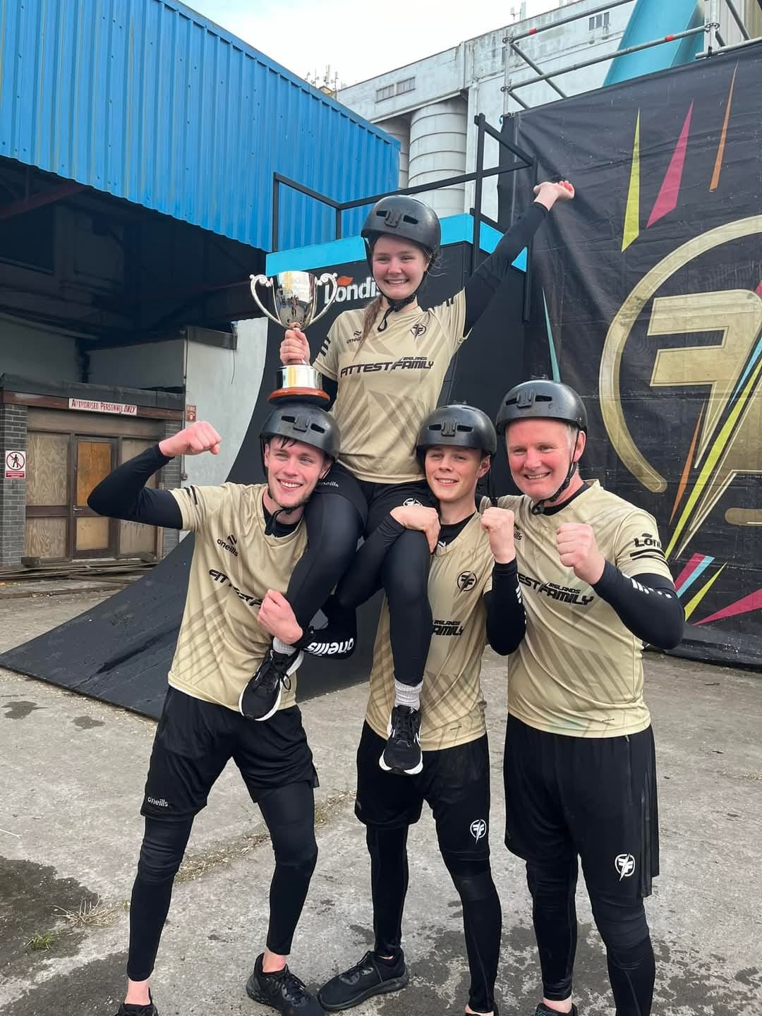 A team of four celebrating with a trophy, one member lifted on the others' shoulders